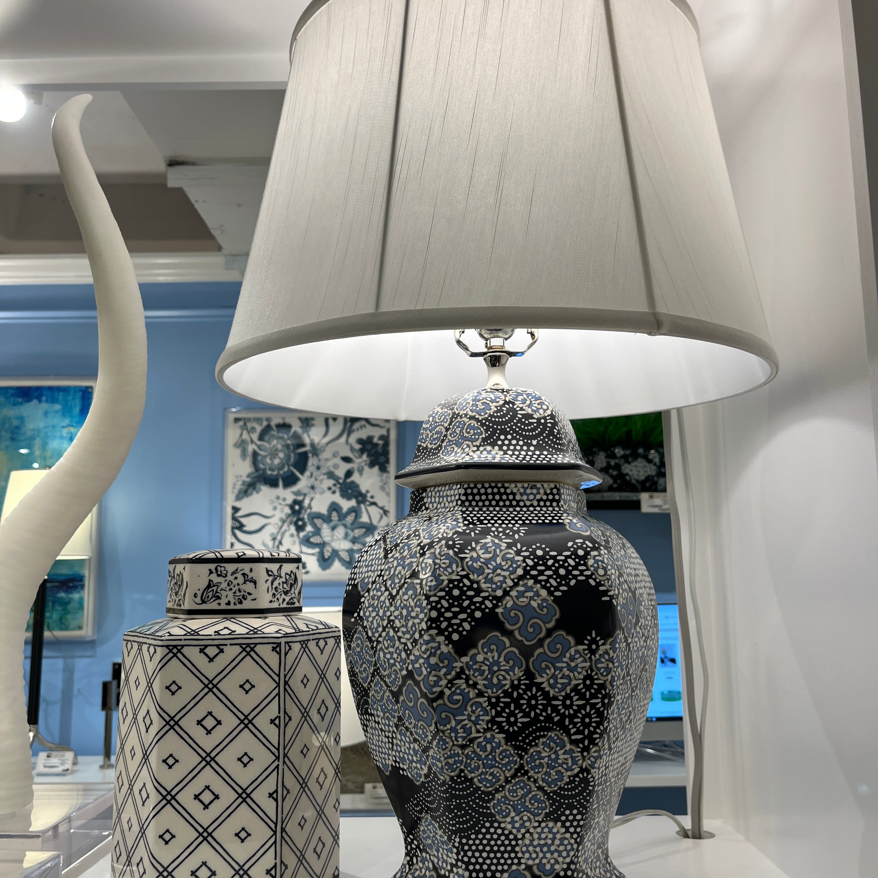 An illuminated navy table lamp with a navy blue patterned base and white shade.