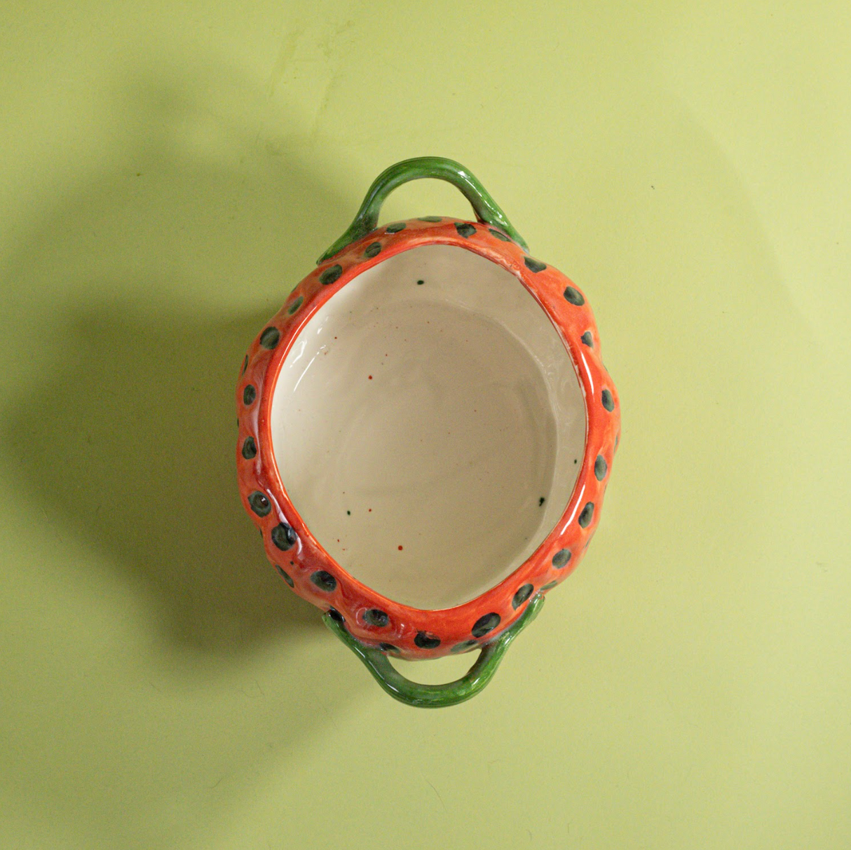 the inside of a large red vintage strawberry dish with a green handles and green detail on lid