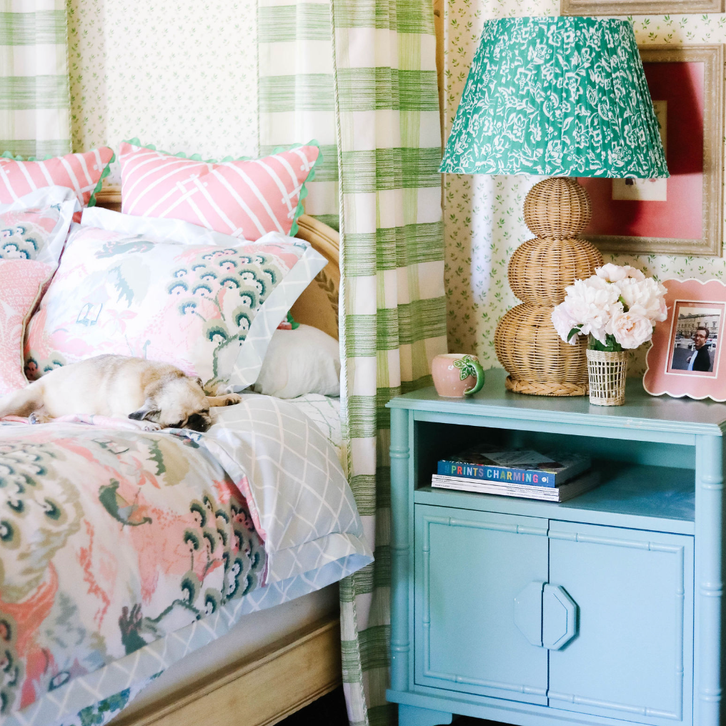 A large rattan lamp with a green lampsade on a blue night stand in a floral bedroom scene. 