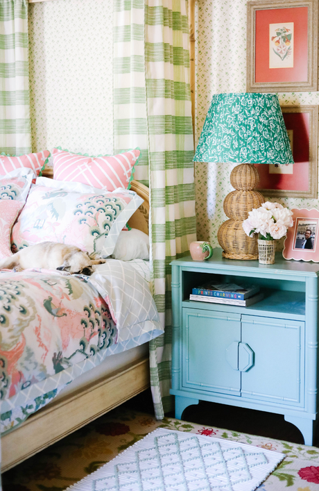 A large rattan lamp with a green lampsade on a blue night stand in a floral bedroom scene. 