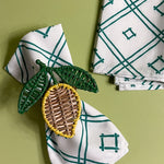 white and green dinner napkins in Island House Small trellis print madcap cottage fabric held with a lemon napkin ring against a light green background

