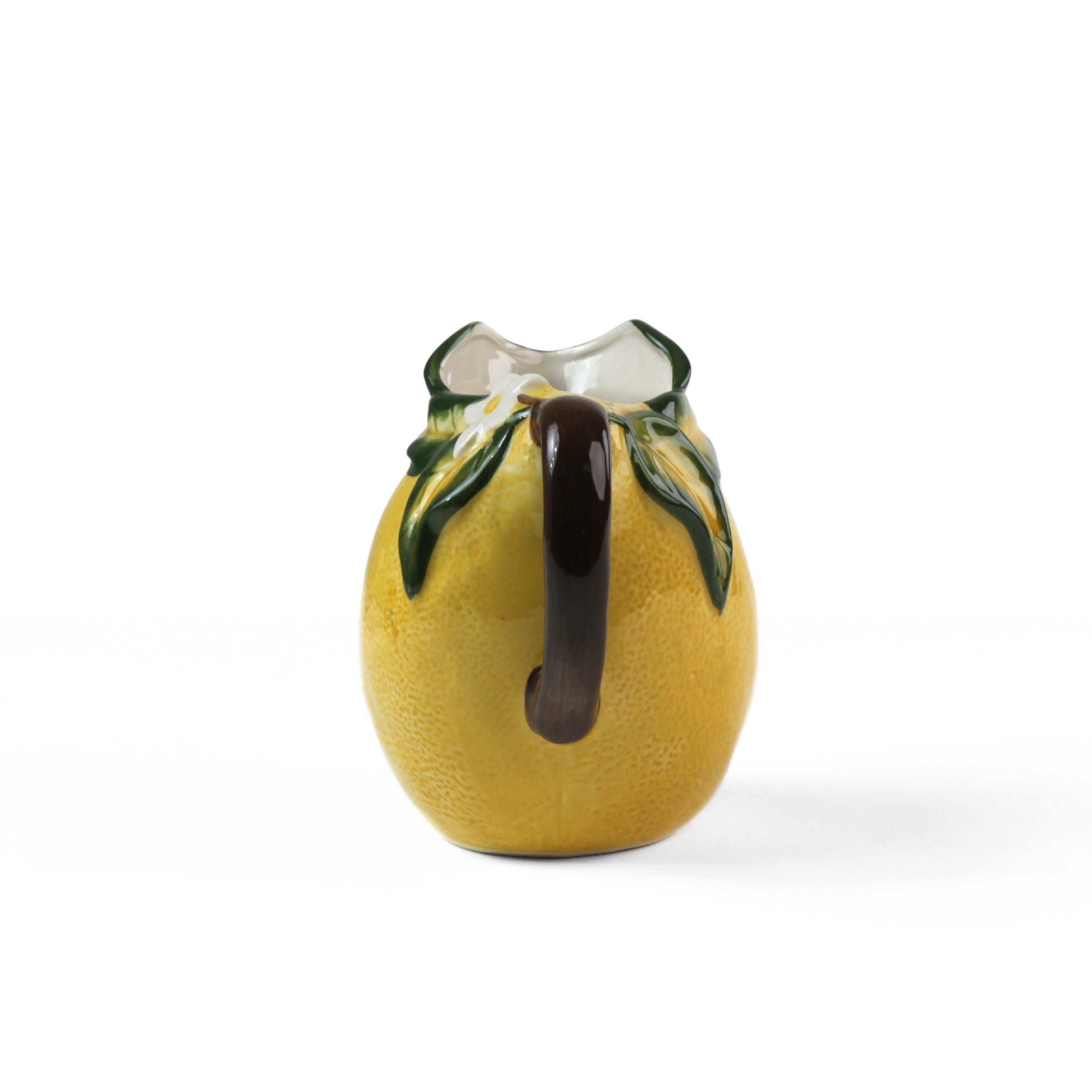 Lemon pitcher yellow ceramic handle view with textured lemon body, green leaf details, and dark curved handle.