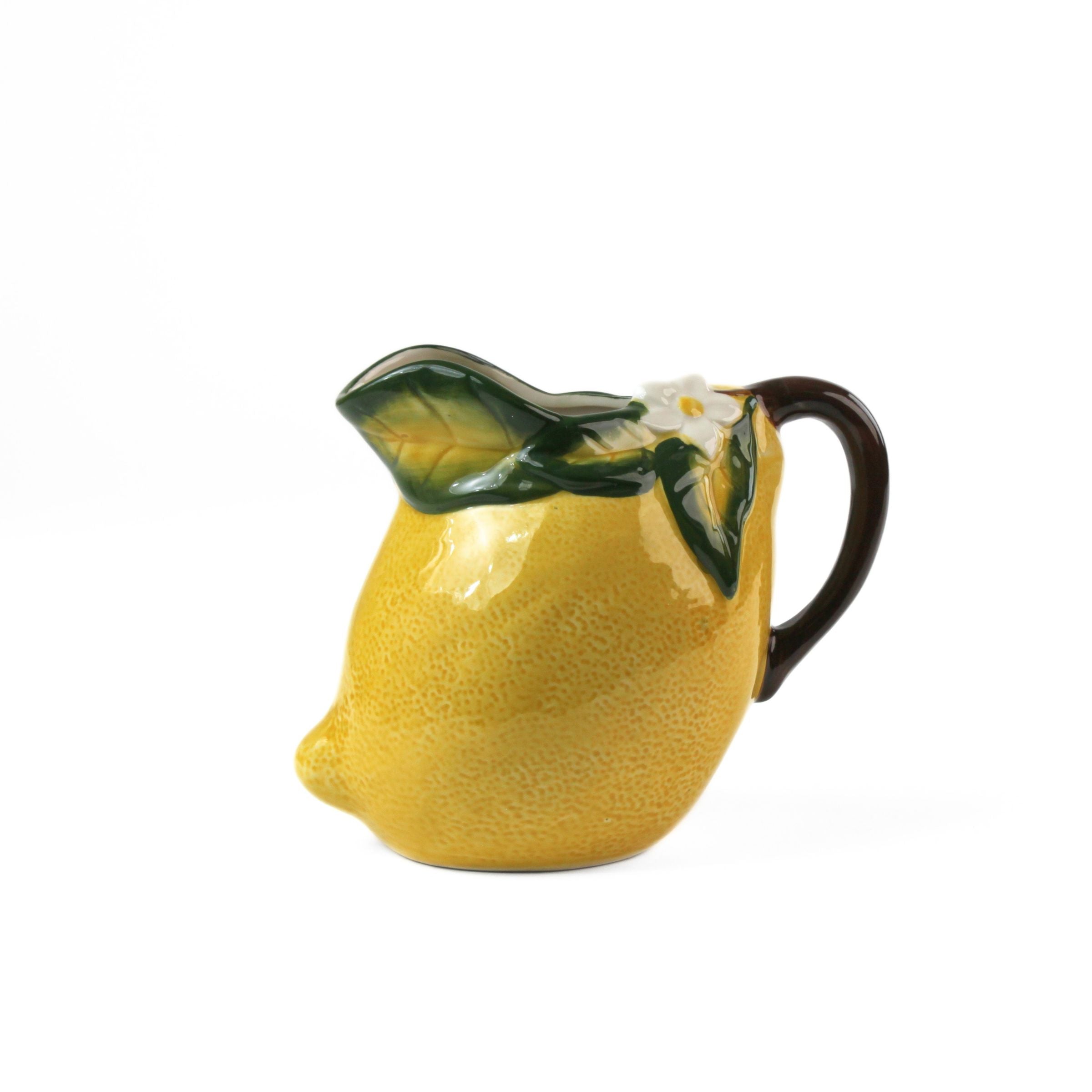 Lemon pitcher yellow ceramic main view with green leaf details and curved dark handle on a white background