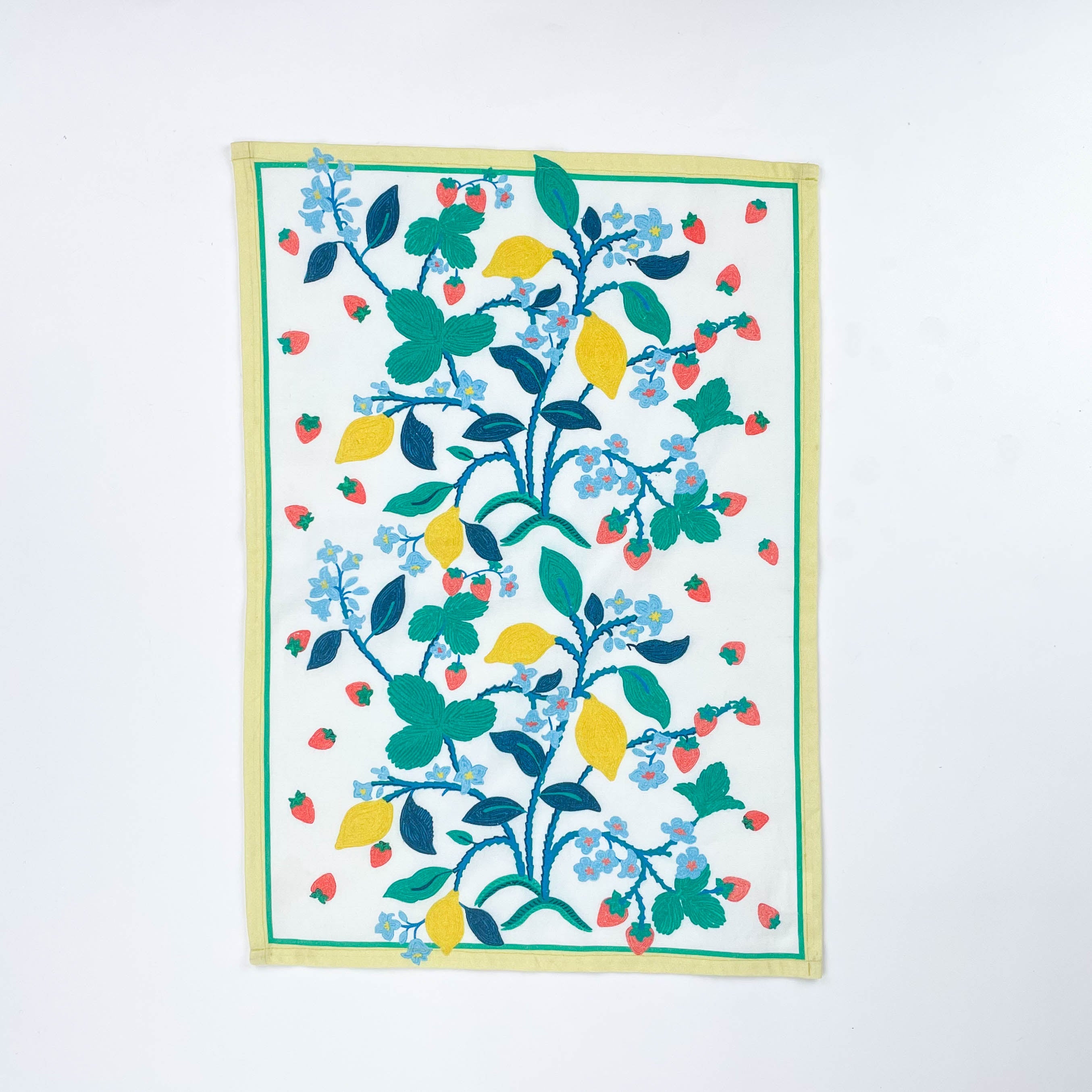 Christmas tea towel featuring a bright botanical design with yellow lemons, red strawberries, and green leaves on a white background bordered with soft yellow and green trim.