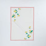 White Christmas tea towel decorated with yellow lemons and green leaves along the edges, bordered by a thin red outline