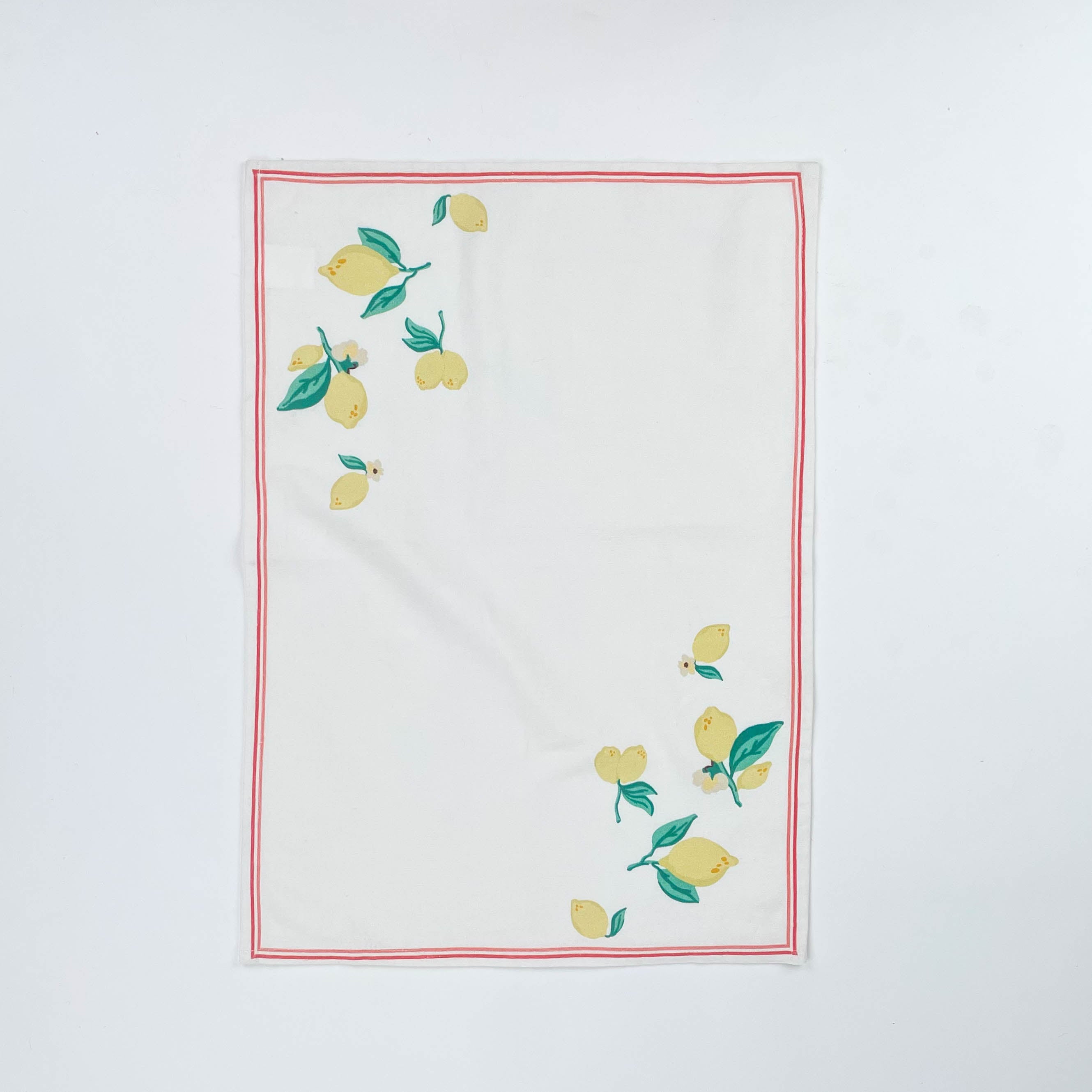 White Christmas tea towel decorated with yellow lemons and green leaves along the edges, bordered by a thin red outline
