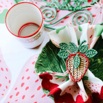 a strawberry fabric table runner topped with a cabbage plate, strawberry napkin and rattan napkin ring