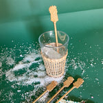 a gold pineapple drink stirrer in a ice filled glass on a green background. 