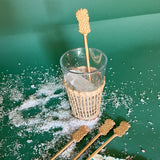 a gold pineapple drink stirrer in a ice filled glass on a green background. 