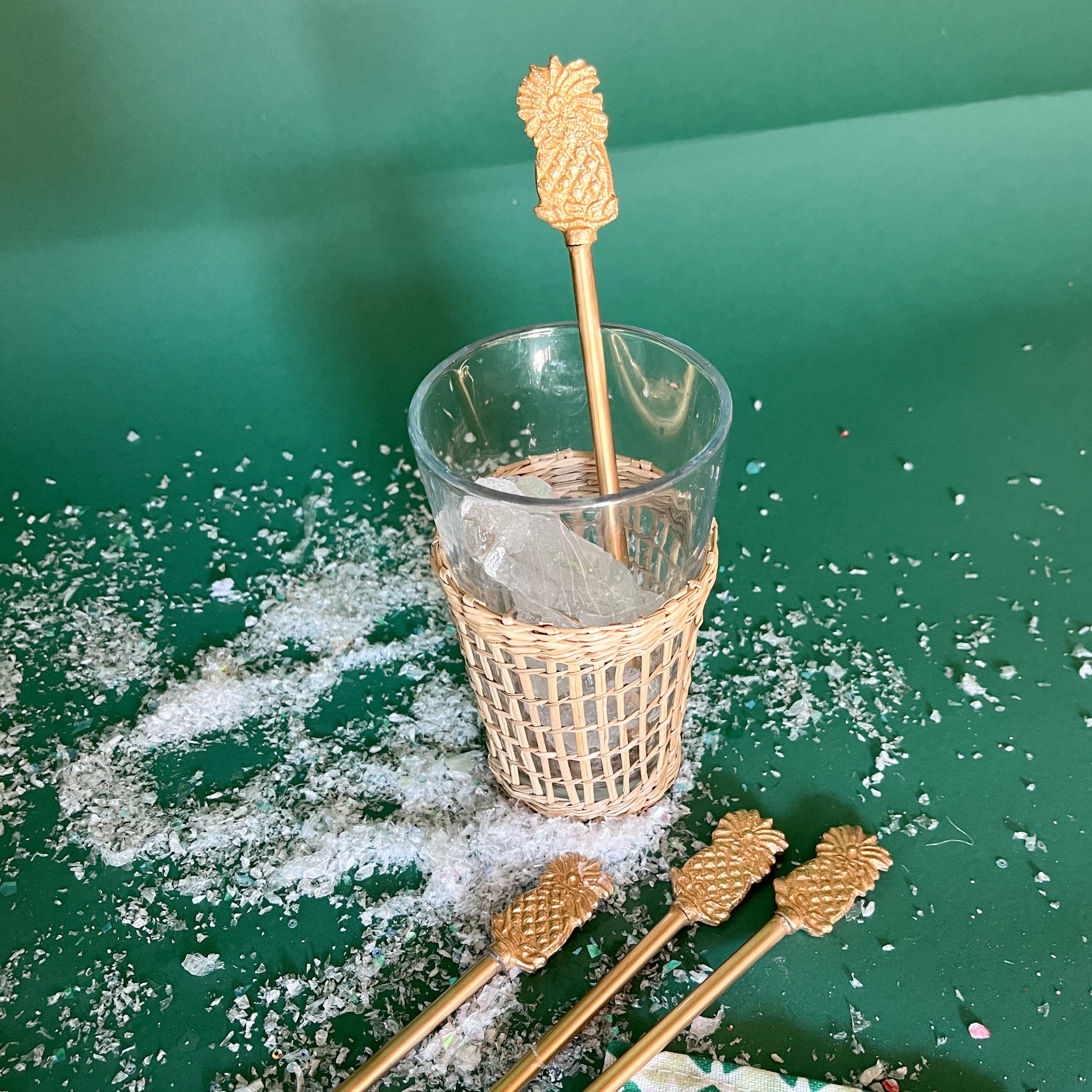a gold pineapple drink stirrer in a ice filled glass on a green background. 