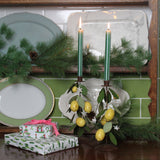 a pair of tole metal lemon candle holders with lit green striped candles next to two wrapped gifts on a wooden cabinet