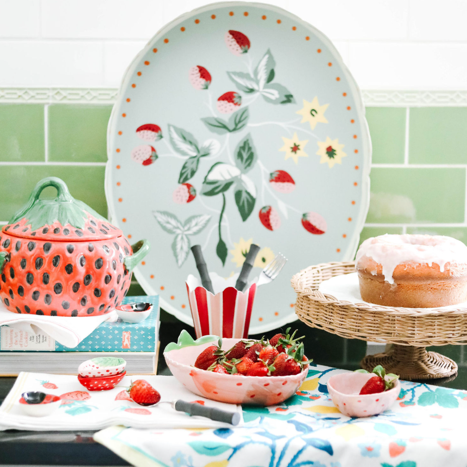 A kitchen scene featuring strawberry decor products such as a strawberry tray strawberry bowls, small strawberry dishes and strawberries and cake.