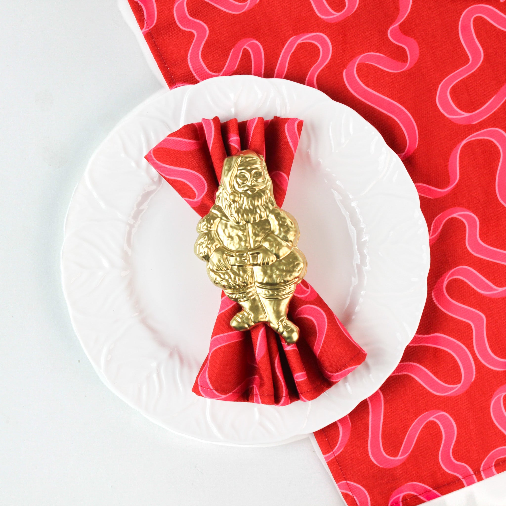 Gold Santa napkin ring holding a red squiggle napkin on a white plate, festive holiday table setting accent perfect for Christmas tea towel styling, seasonal entertaining, and Christmas table décor