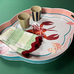 Lifestyle image of rock lobster pink and green tole metal tray with two ceramic cups and two Gin Lane dinner napkins with ric rac