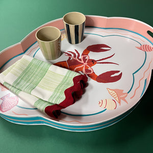 Lifestyle image of rock lobster pink and green tole metal tray with two ceramic cups and two Gin Lane dinner napkins with ric rac