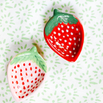 a pair of small ceramic strawbery dishes on a green and white tablecloth
