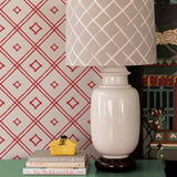 beige lamp agains a wall of red and white wallpaper in a bamboo trellis design.