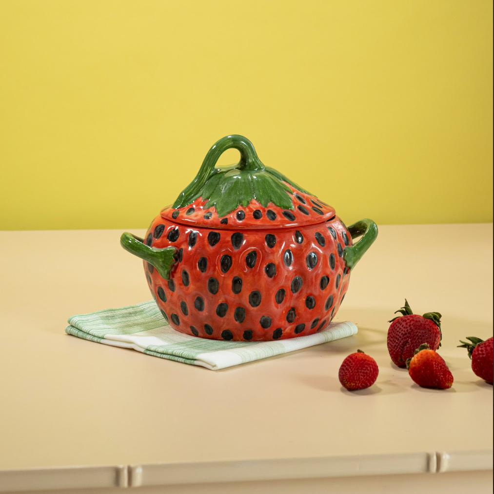 a vintage strawberry bowl on a green and white napkin with strawberries scattered in foreground. 