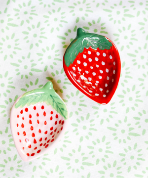 a pair of small ceramic strawbery dishes on a green and white tablecloth