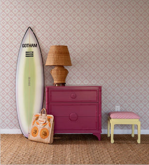 a surfboard and red chest in front of a pink bamboo trellis wallpaper design on a white background from Madcap Cottage