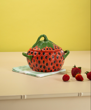 a vintage strawberry bowl on a green and white napkin with strawberries scattered in foreground. 