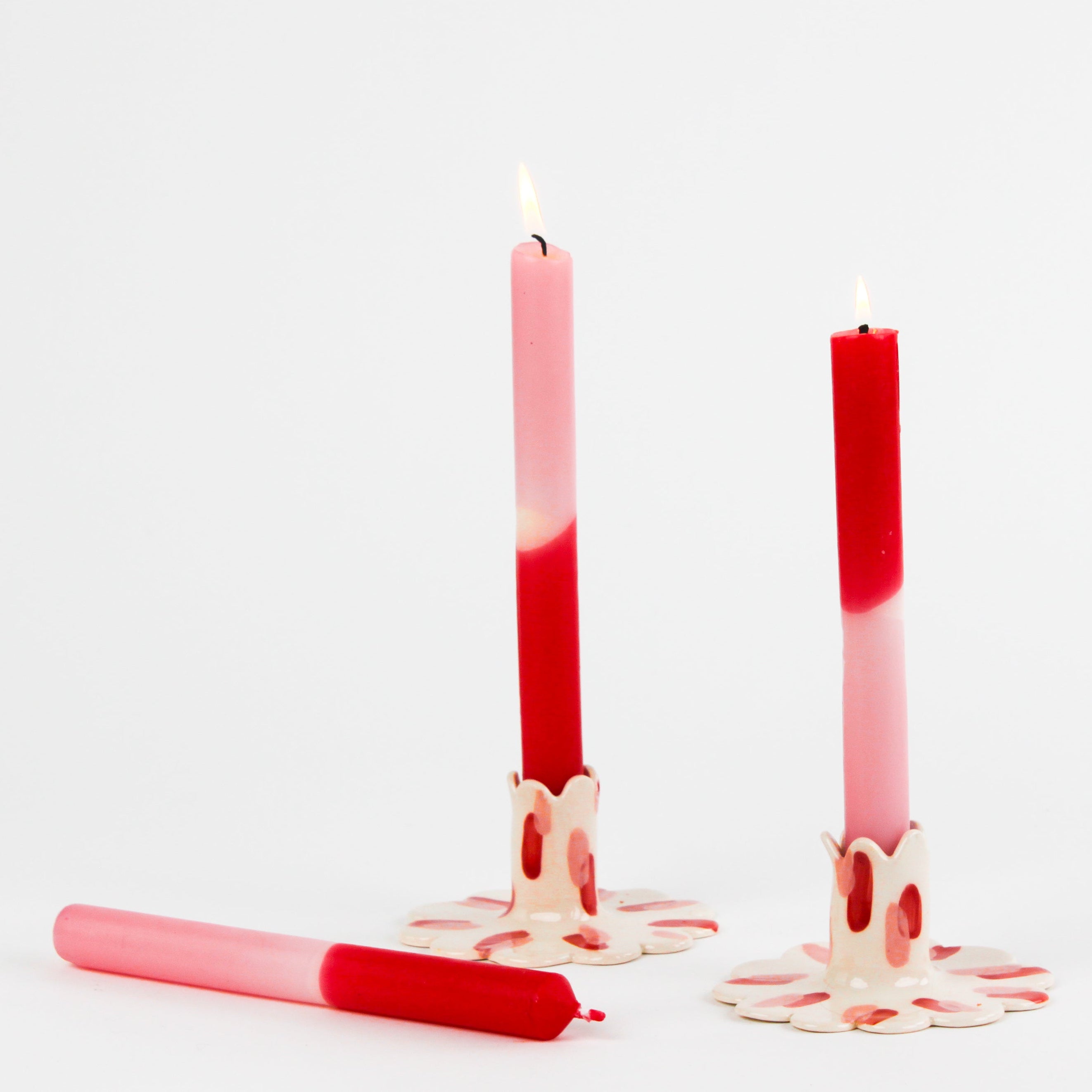 lit 2 pink and white Colored Taper Candles candle holders and 1 lyting horizontally in a white background