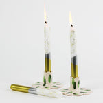 lit Silver and gold taper candles with glitter accents on the upper part of the candle against a white background. 