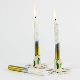 lit Silver and gold taper candles with glitter accents on the upper part of the candle against a white background. 