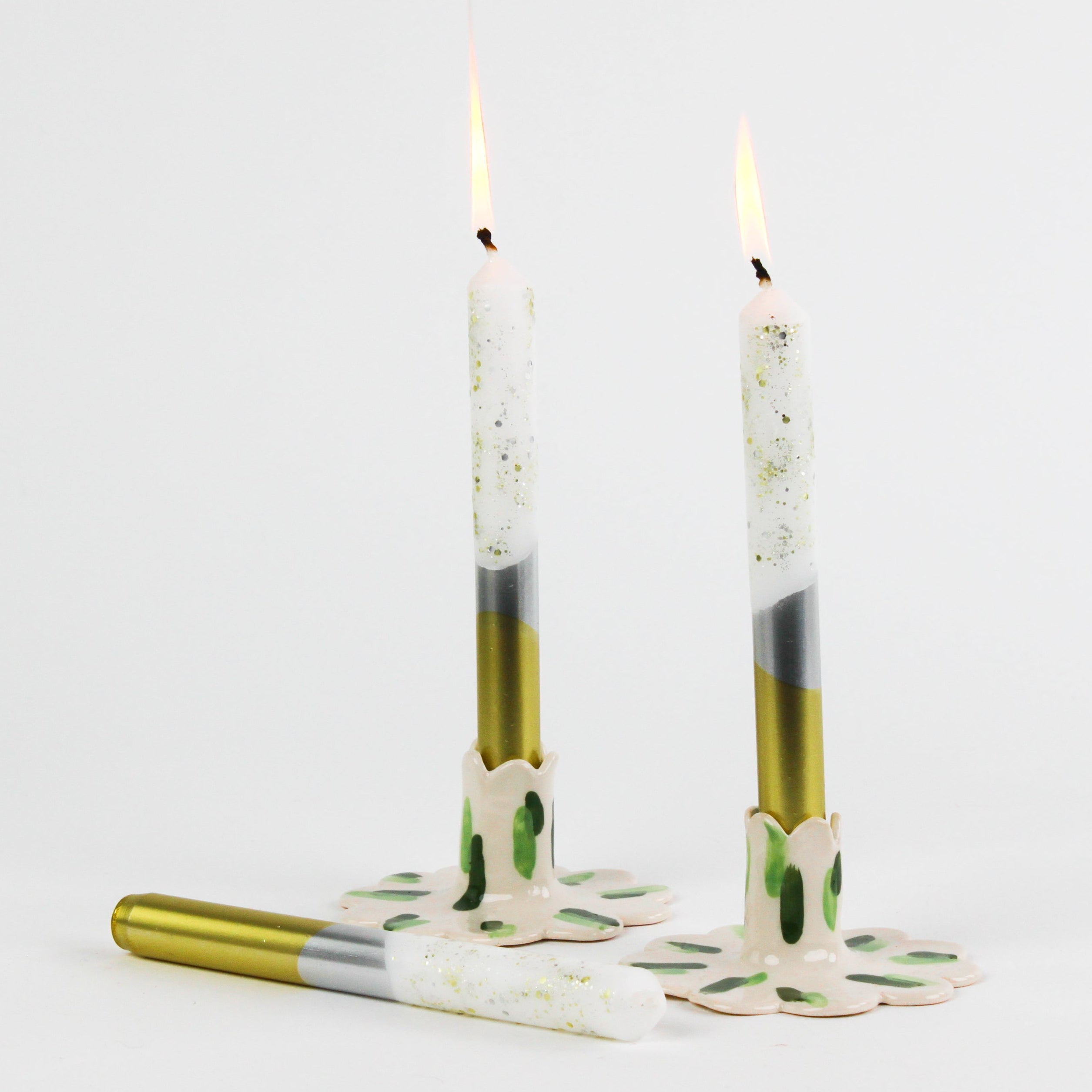 lit Silver and gold taper candles with glitter accents on the upper part of the candle against a white background. 