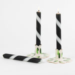 lit 2 white and black striped Taper Candles candle holders and 1 lying horizontally in a white background