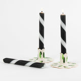 lit 2 white and black striped Taper Candles candle holders and 1 lying horizontally in a white background