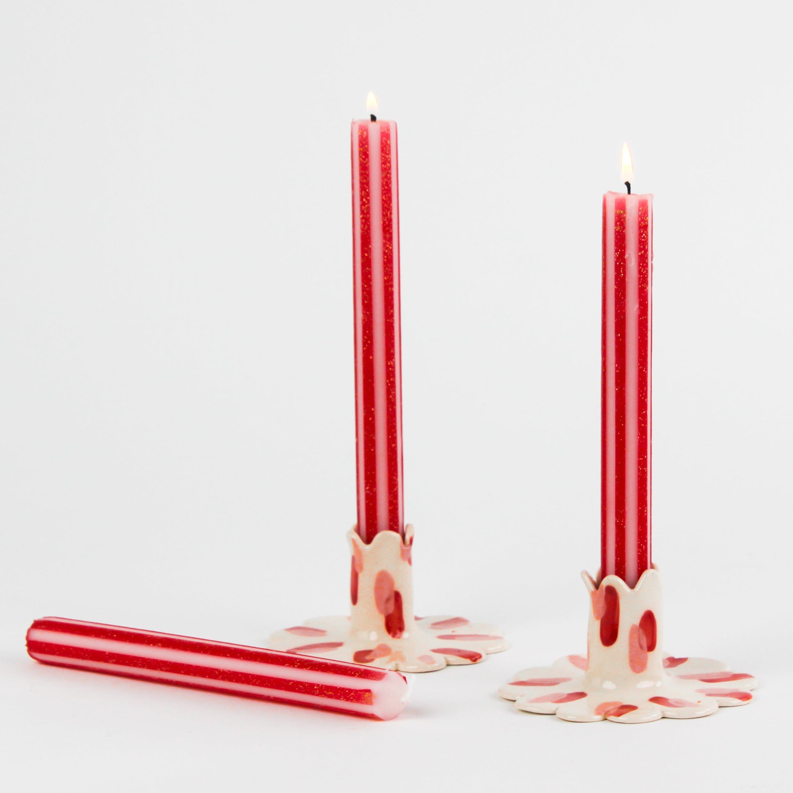 lit 3 gold red and white striped taper candles lying in a white background
