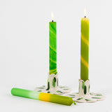 a lit green yellow taper candle in a white/green candle holder