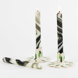 lit 2 marbled white and black Taper Candles candle holders and 1 lying horizontally in a white background