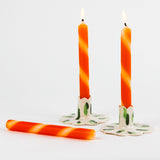 lit Three orange and white stripe taper candles in white background