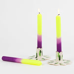 lit 2 taper candles with a purple and yellow gradient with 1 laying down in a white background