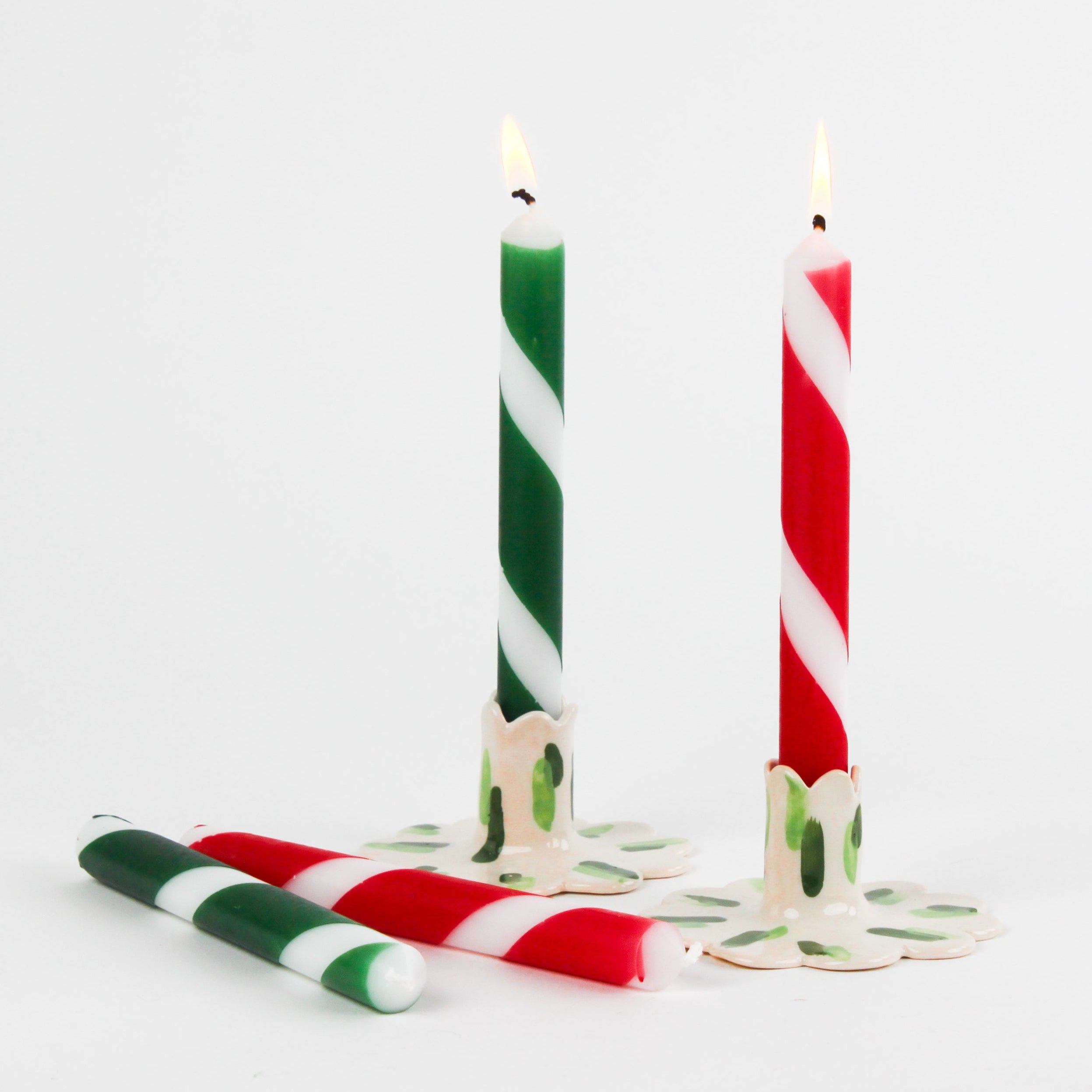 3 set lit candles of red, green, and white striped christmas taper candles on a white background