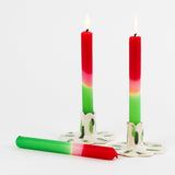 lit 2 Red Pink Taper Candles and another one laying down in a white background