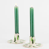 lit 2 style gold green pinstripe taper candles in a holder with white background
