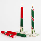 lit 4 red and green taper candles with varied stripe designs on a white background. 