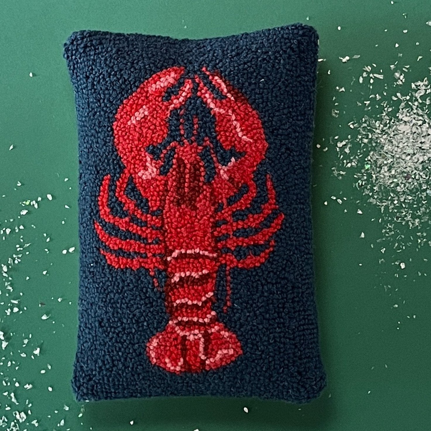a navy blue hooked wool pillow with a central large red lobster motif