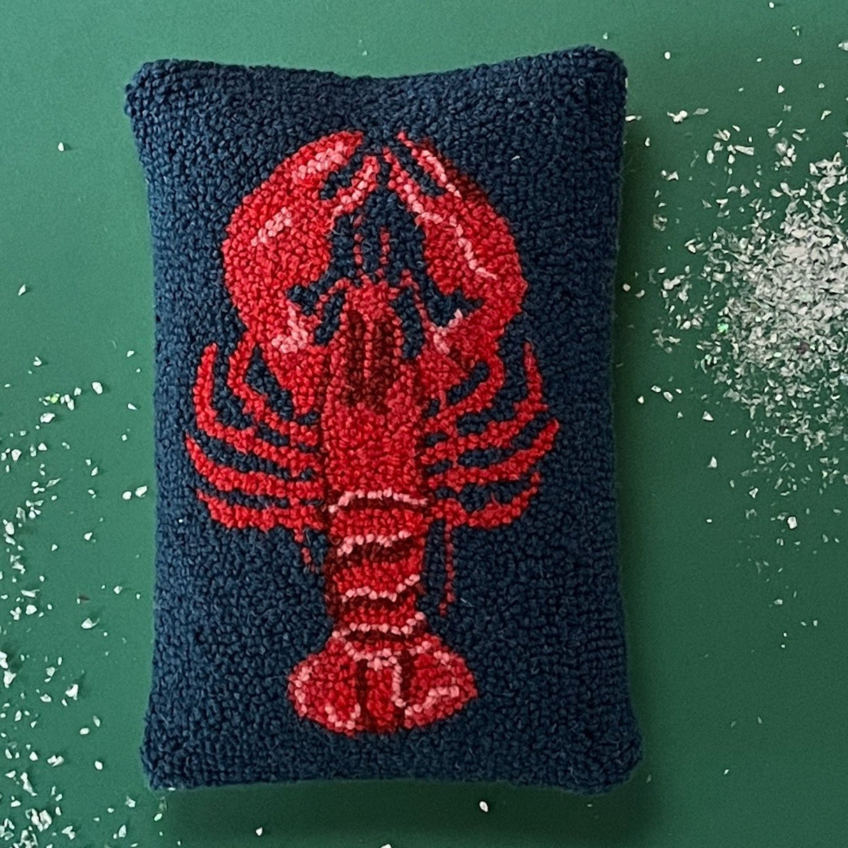 a navy blue hooked wool pillow with a central large red lobster motif
