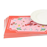 Stacked coastal themed paper placemats with lobster, shells, florals, and fruit illustrations beside a white textured dinner plate.