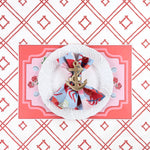 A styled coastal table setting featuring a lobster themed paper placemat, white plate, nautical napkin with anchor ring, and coral trellis patterned background.