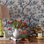 A desk featuring a tulip filled vase against blue and white chinoiserie wallpaper