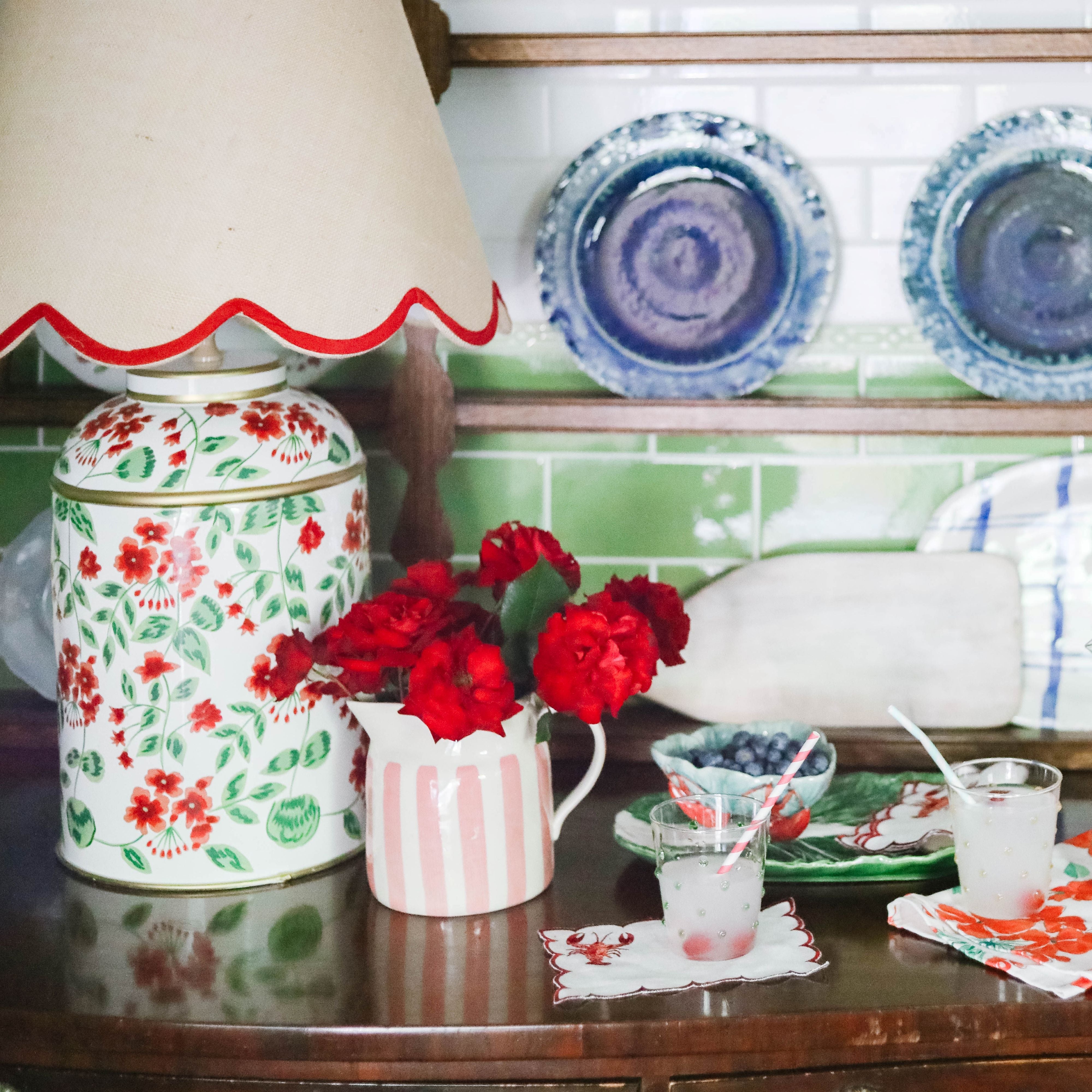 Kitchen counter styled with floral canisters, patterned glassware, green tile backsplash, and red floral accents.