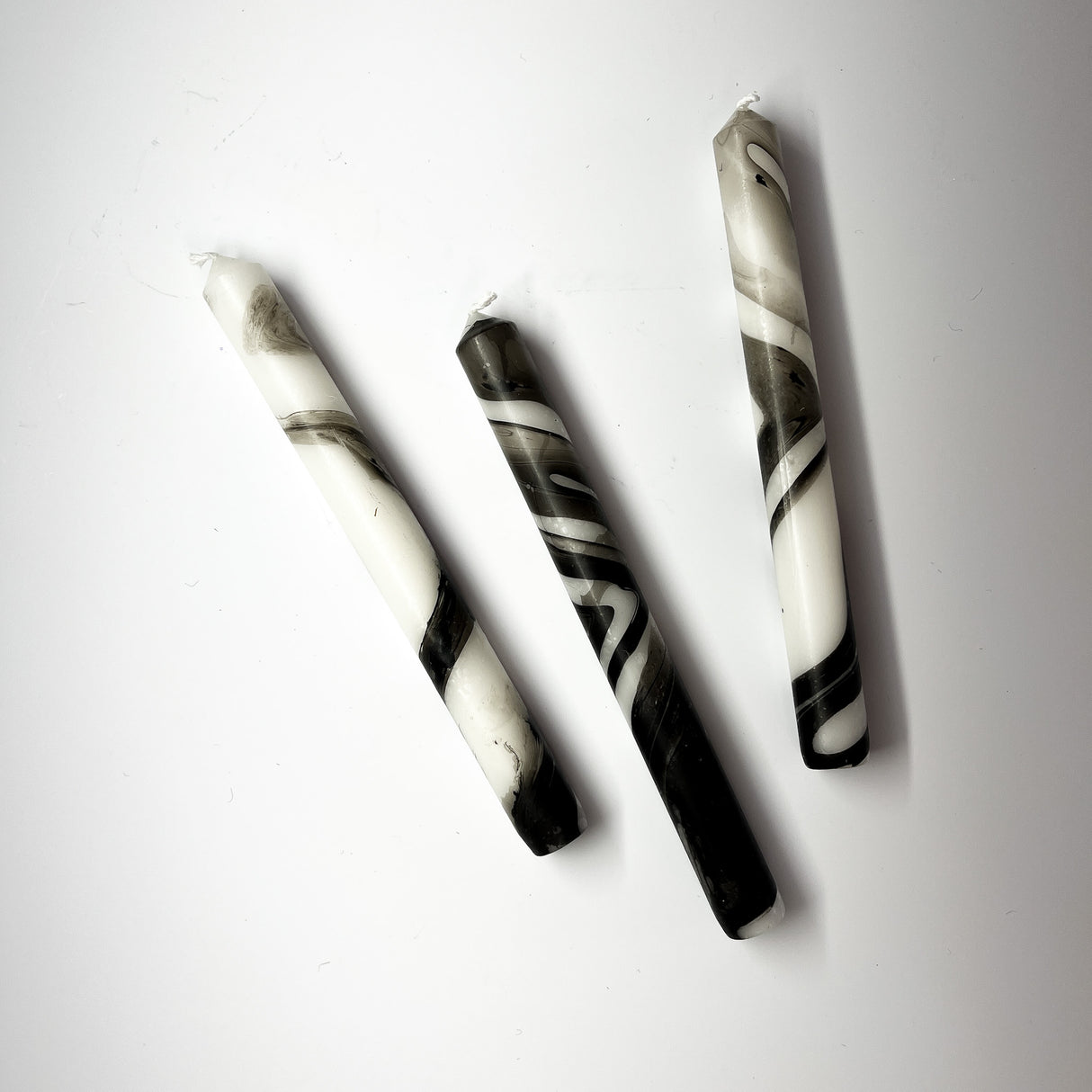 Three marbled black-and-white taper candles are lying horizontally.