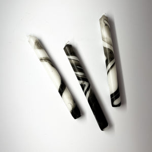 Three marbled black-and-white taper candles are lying horizontally.