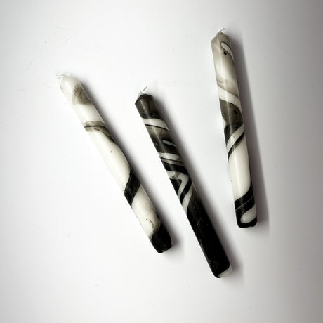 Three marbled black-and-white taper candles are lying horizontally.