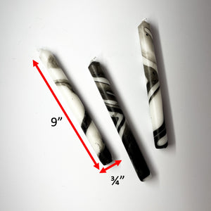 Three marbled black-and-white taper candles on a light background, lying horizontally. Dimensions are 9" by 3/4"